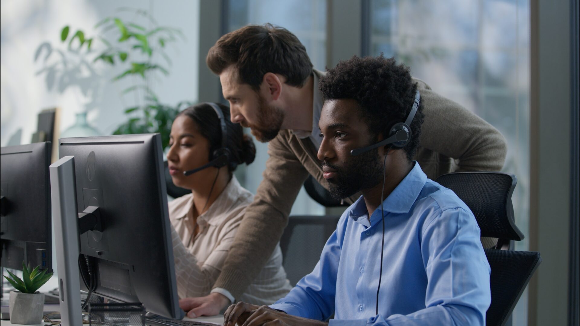 Callcenter teamwork multicultural office operators support communication African man Indian woman headset computer helpdesk Caucasian supervisor pointing monitor giving instructions customer service